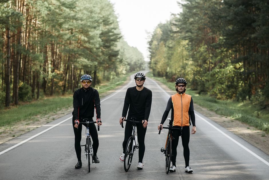 Trois cyclistes arrêtés côte à côte sur une route bordée d'arbres